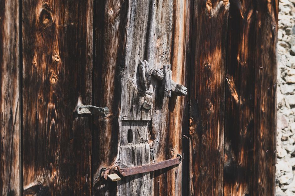 Close-up of a weathered wooden door featuring a vintage lock in a rustic setting.