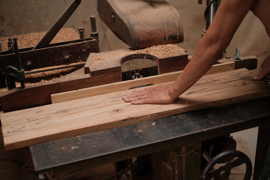 A carpenter skillfully operating a wood planer, shaping a wooden board in a workshop setting.